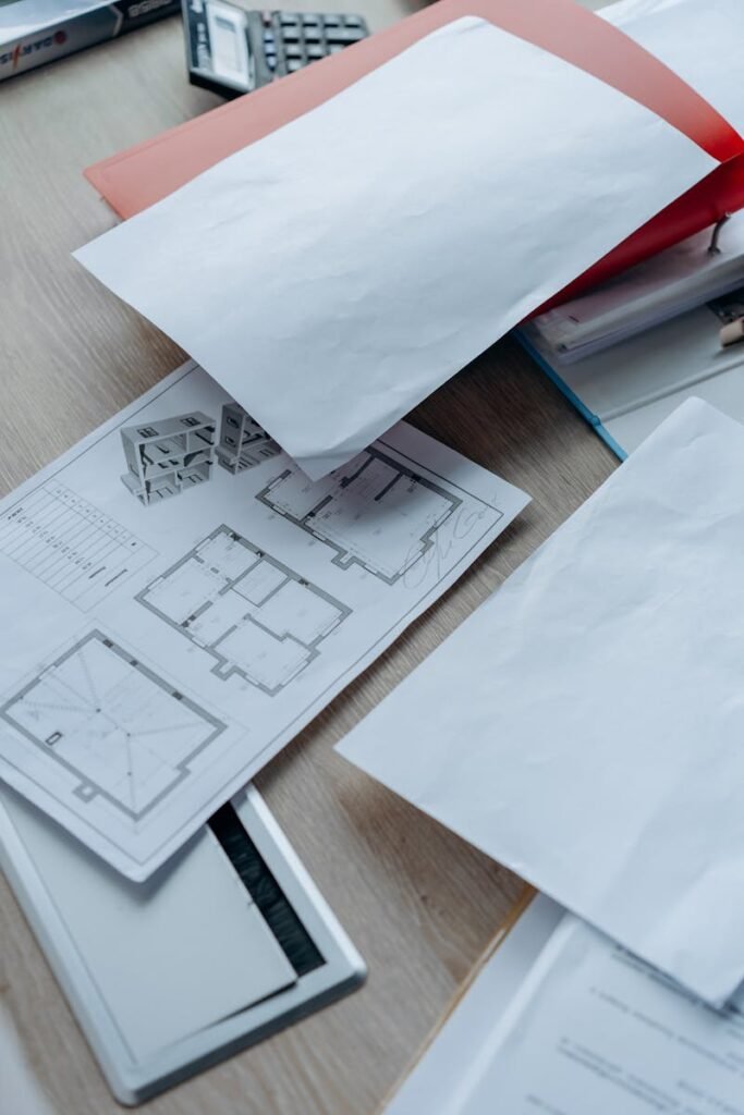 High angle view of architectural floor plans and paperwork on a wooden desk in an office setting.